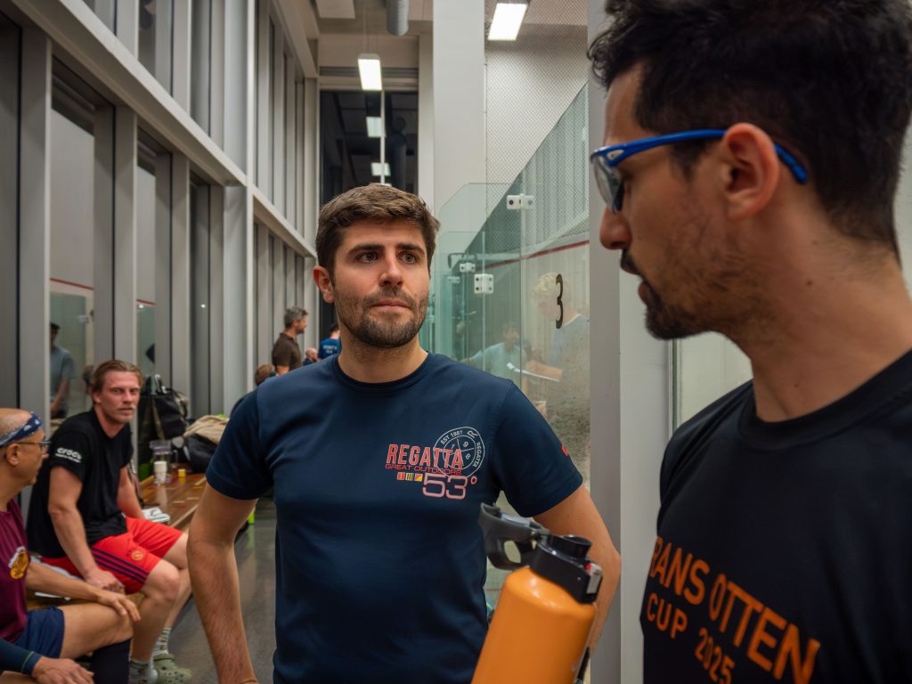 Two club members chatting beside the glass squash court.