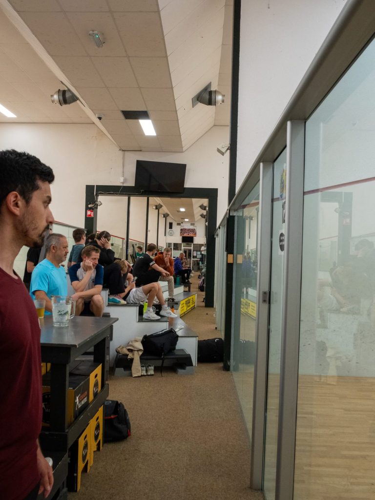 Spectators watching league squash from the corridor beside the courts.