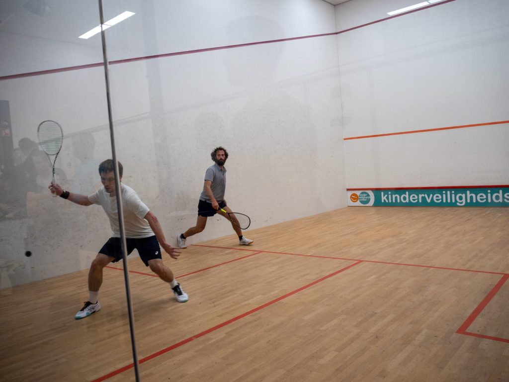Two players contest a rally near the glass side wall.