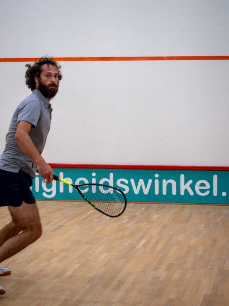 A player in a grey shirt watches the ball with racket ready.
