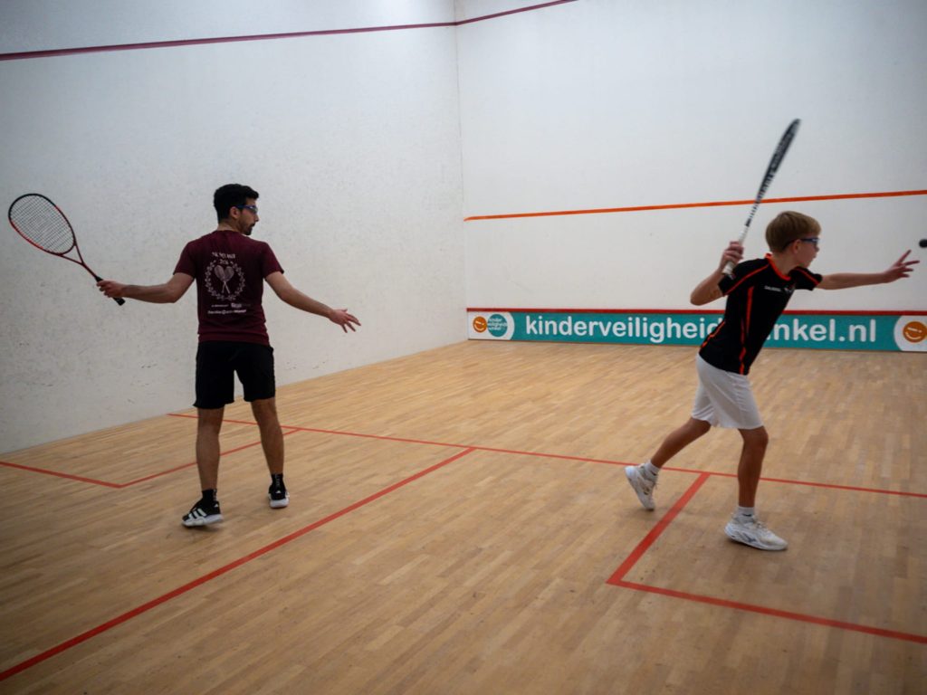 Two players in burgundy and black shirts contest a rally on the squash court.
