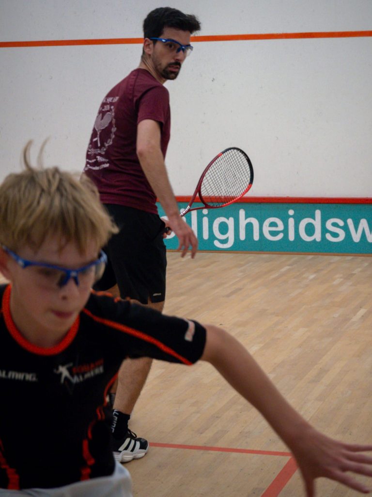 Two players track the ball during a squash rally.