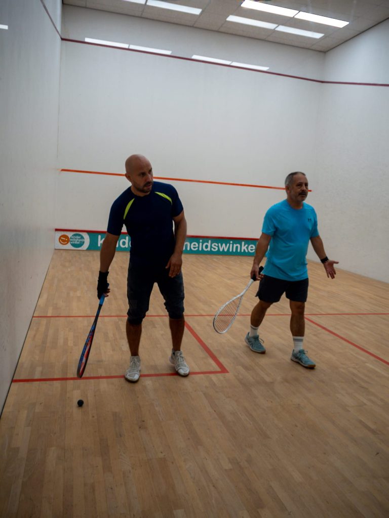 Two players in blue shirts wait with their rackets on court.