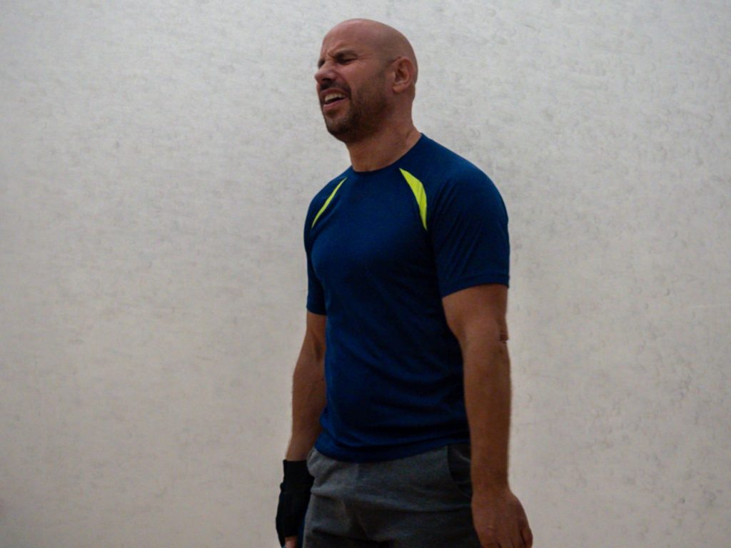 A player in a navy and yellow shirt watches play on court.