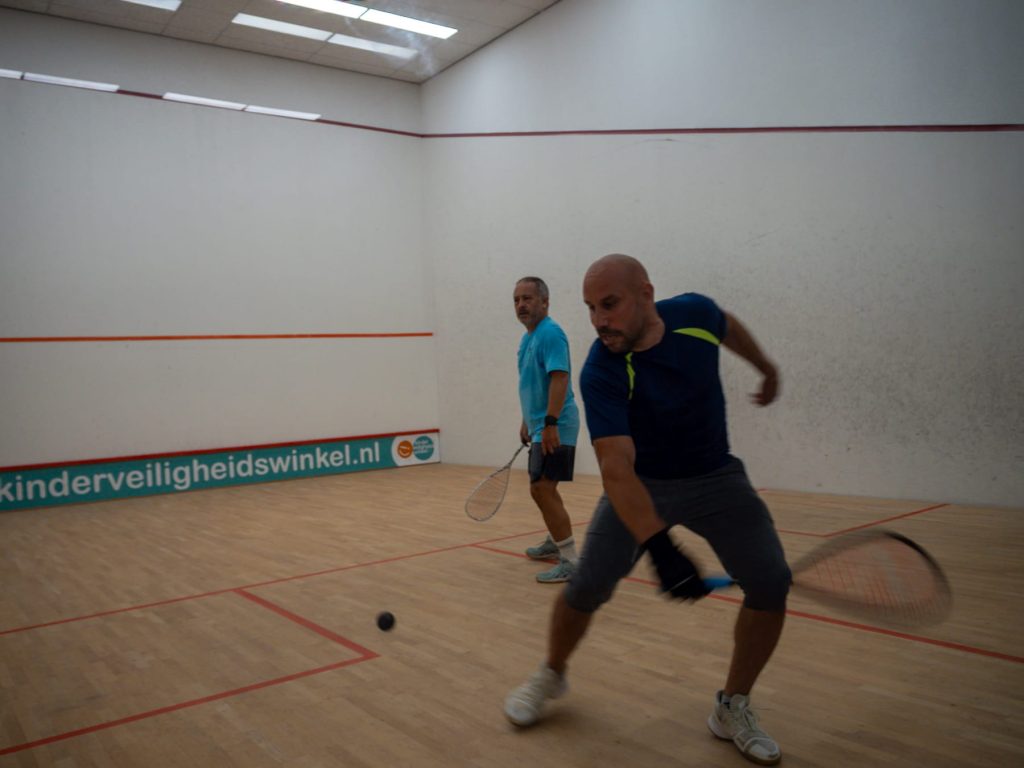 A player reaches low to return the ball while an opponent watches.