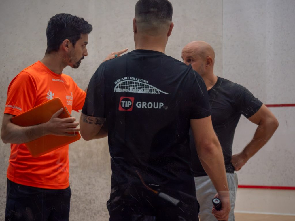 Three players talking together on the squash court.