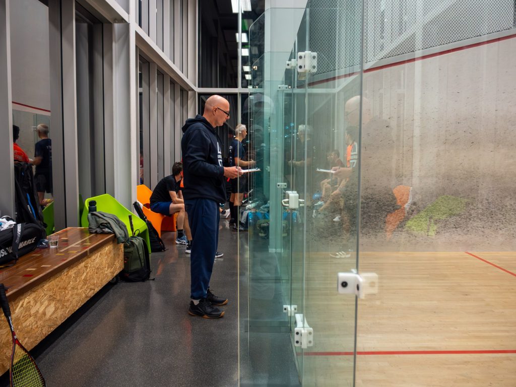 A spectator standing beside the glass court with a drink.