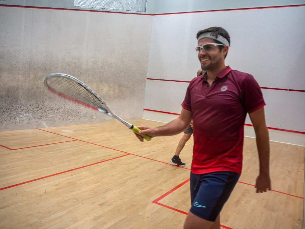 A smiling player in burgundy and protective eyewear holding his racket on court.