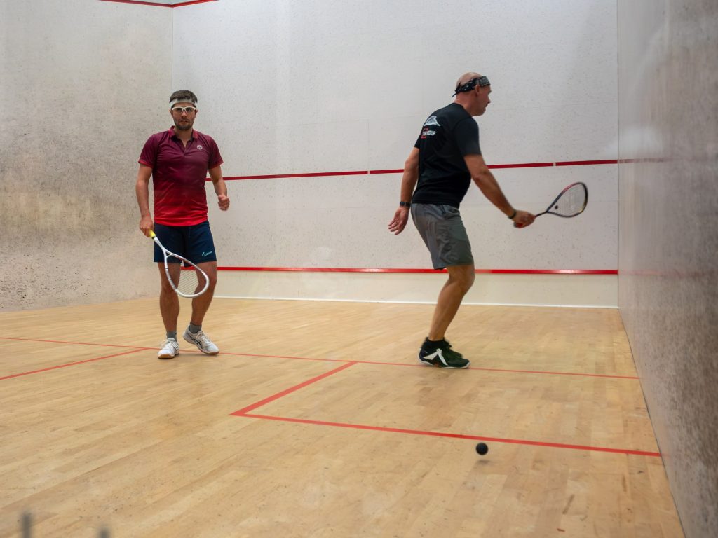 Two players with rackets on the squash court between rallies.