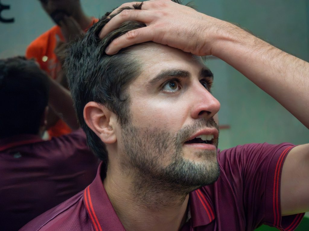 A player in burgundy resting beside the court with a hand on his head.