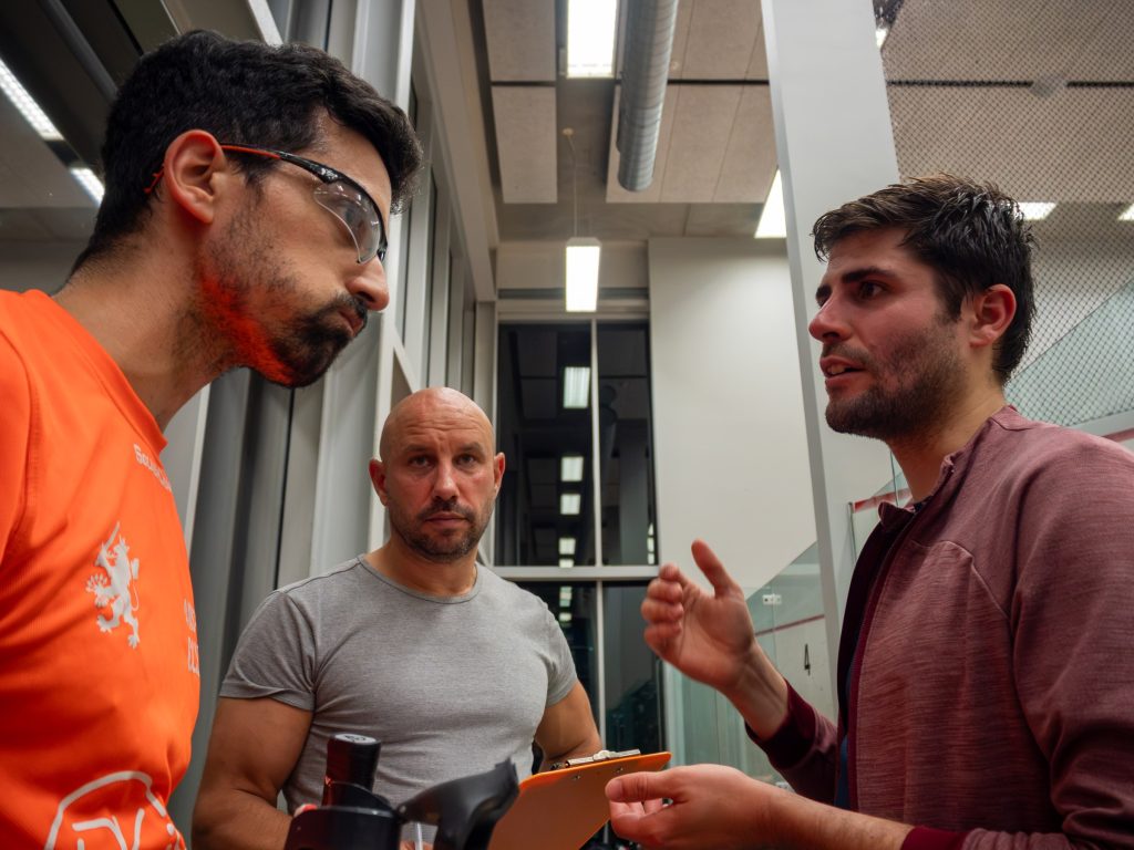 Three players talking beside the glass court.