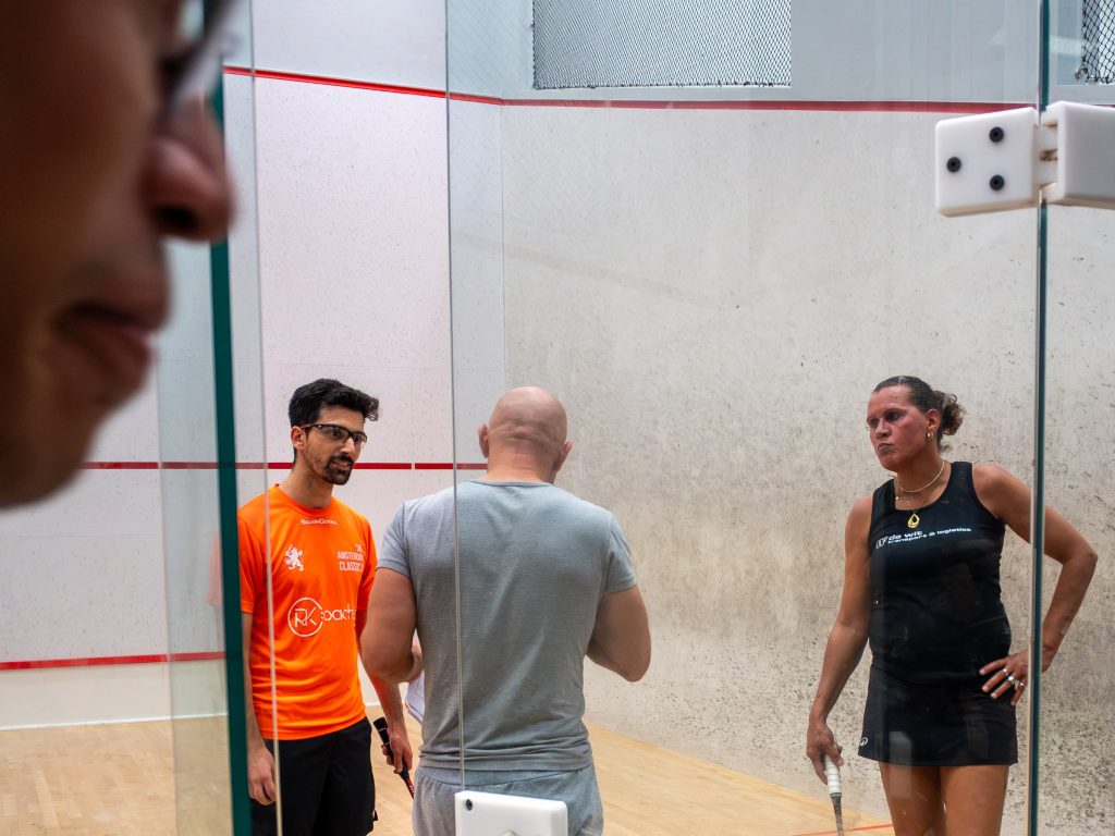 Three players talking together at the glass court door.