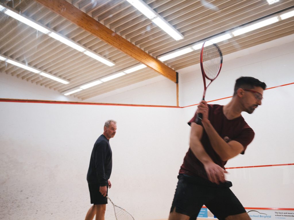 A player in a burgundy shirt preparing a racket shot with his opponent behind him.