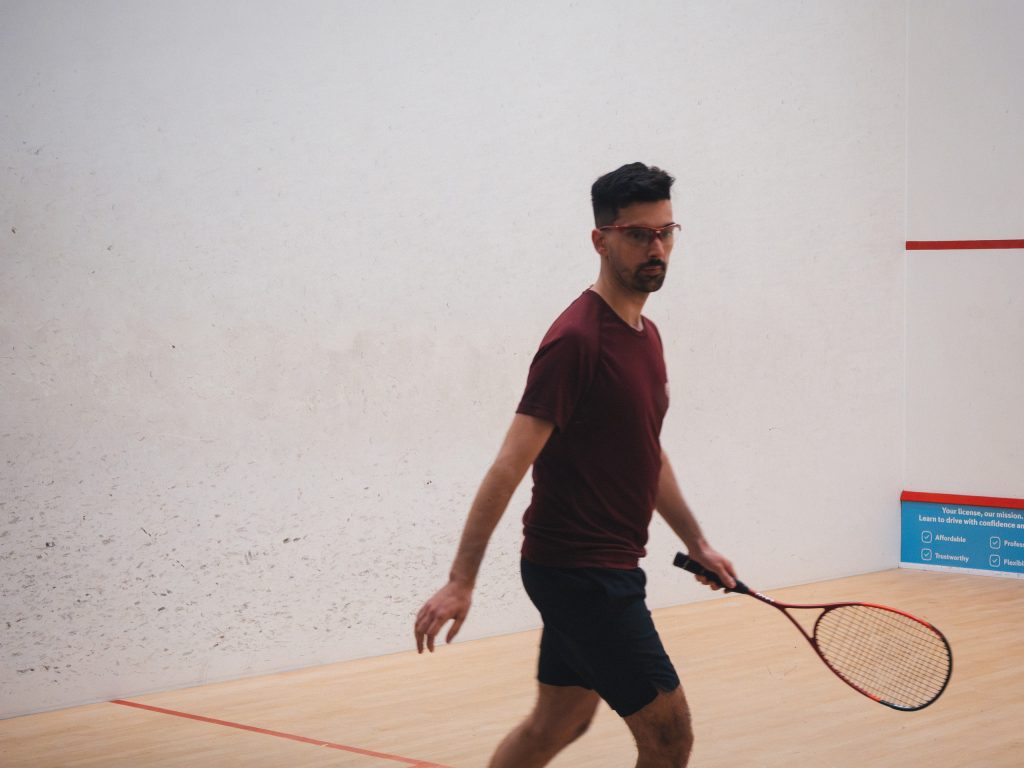 A player in a burgundy shirt holding his racket and turning on the squash court.