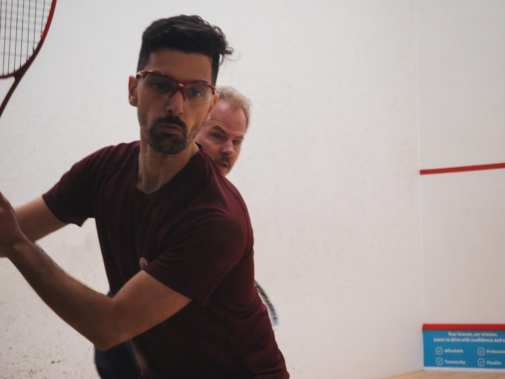A player in protective eyewear and a burgundy shirt preparing to strike the ball.